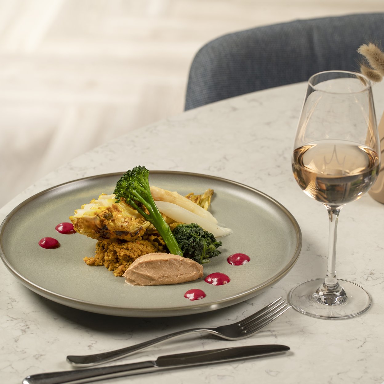 Raffiniertes Restaurant-Gericht mit Quinoa, grünem Gemüse und Spargel, serviert mit Weißwein auf Marmortisch.